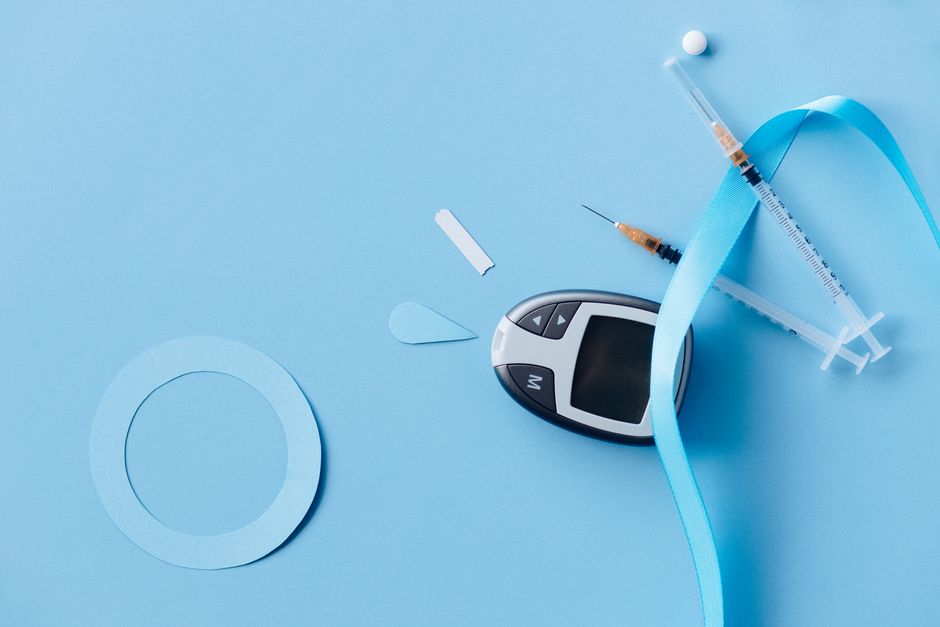 Flat lay of a diabetes monitoring kit with syringes and glucose meter on a blue background.