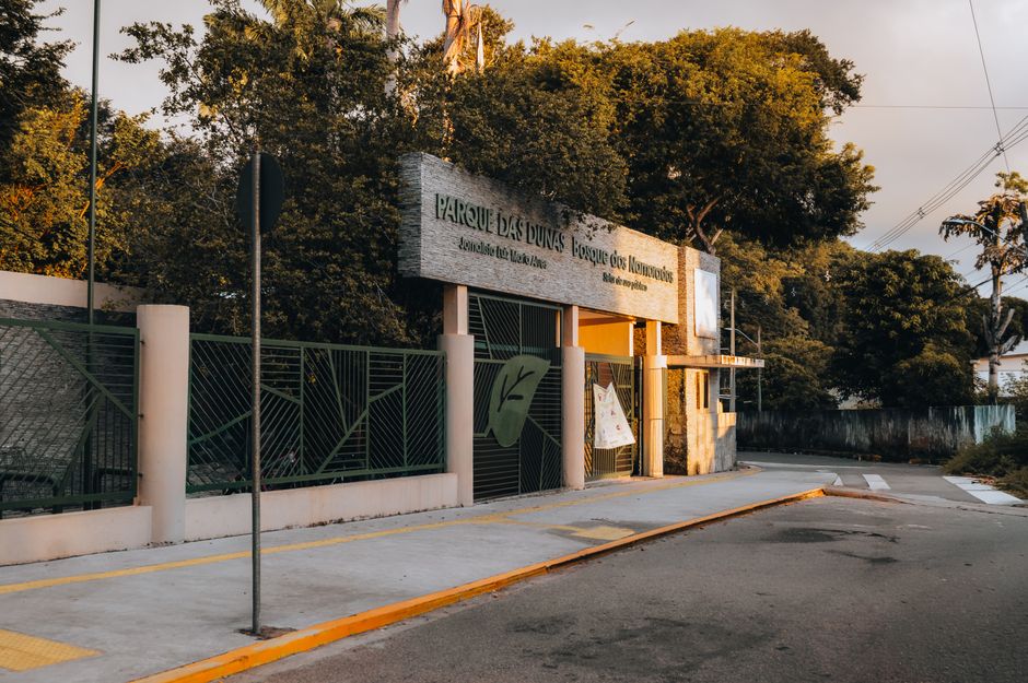 Sunlit entrance of Parque das Dunas in Natal, RN, showcasing greenery and architectural design.