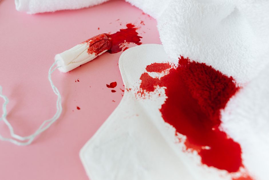 A sanitary pad and tampon with blood stains on a pink surface, highlighting menstruation concepts.
