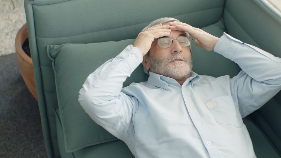 A senior man with eyeglasses relaxing on a sofa, looking stressed and tired.