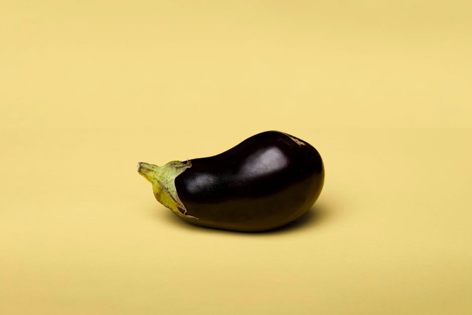 A single eggplant on a clean yellow background, captured in a minimalist style.