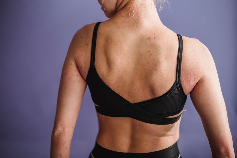 Back view of crop anonymous female in black sportive underwear standing against purple background in studio
