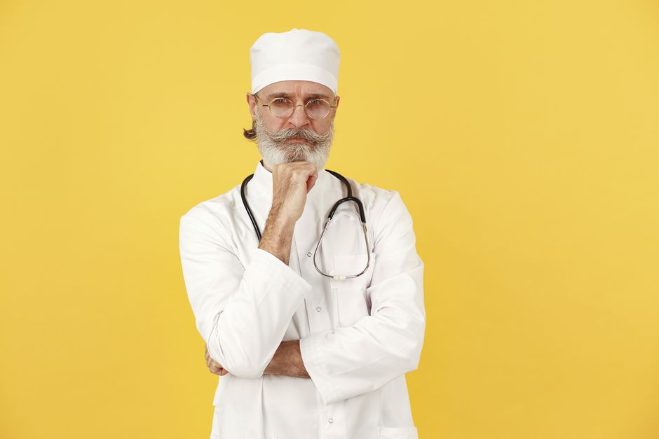 Portrait of a senior male doctor with eyeglasses and stethoscope against a yellow background.