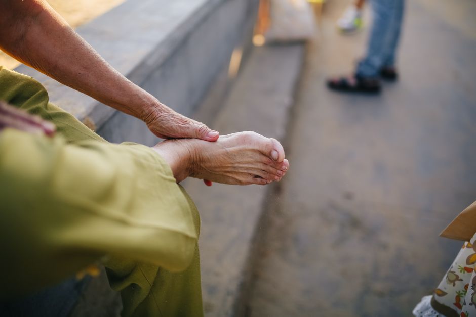 An elderly person sitting outdoors massaging their foot for relief.