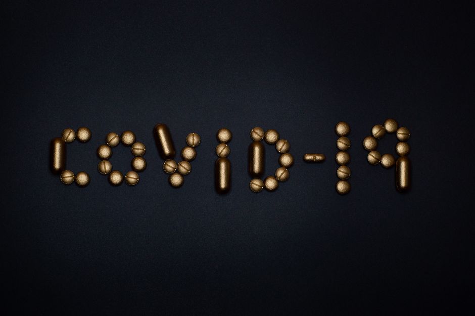 Artistic representation of COVID-19 using golden pills on a black background, symbolizing healthcare and treatments.