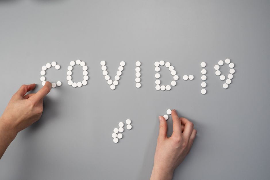 Hands arranging white pills to spell 'COVID-19' on a gray surface, symbolizing medical and health themes.