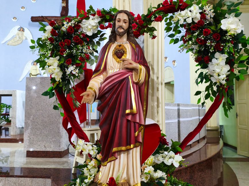 A beautiful statue of the Sacred Heart of Jesus adorned with flowers in a church setting.